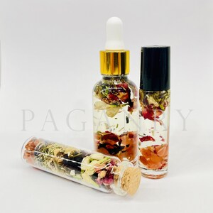 May include: Three glass bottles filled with clear liquid and dried flowers and crystals. The bottles have different shapes and sizes. The bottles are on a white surface.
