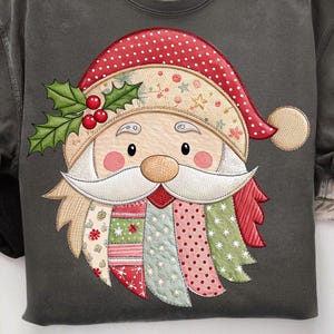May include: Dark gray sweatshirt featuring a colorful Santa Claus face design. The Santa face has a red and white polka-dot hat, a white beard, and a patchwork design with holly and berries. A festive holiday-themed apparel item.