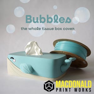 Op de afbeelding: Een lichtblauwe walvisvormige tissueboxhoes met een witte basis en een uitloop van witte tissues. De tekst "Bubbles the whale tissue box cover" staat boven de doos. Een spoel blauw filament staat naast de doos.