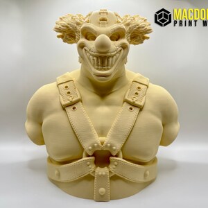 May include: A 3D printed bust of a clown with a menacing grin, wearing a leather harness with buckles and straps. The clown has a large, red nose and wild, orange hair.