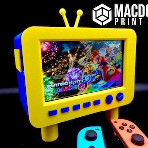 Puede incluir: Un televisor retro amarillo y azul con una pantalla que muestra el videojuego Mario Kart 8 Deluxe. Dos mandos de Nintendo Switch están en primer plano.