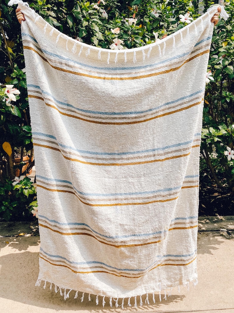 Beach blanket made from upcycled cotton, perfect for beach days, picnics, or yoga. This colorful Mexican blanket is a versatile outdoor blanket, ideal for summer adventures, camping, or as a cozy home decor throw. Soft, lightweight, and eco-friendly, it doubles as a boho throw blanket, blanket gift, or decorative layer for any coastal space. Handwoven by artisans, this sustainable, upcycled cotton blanket adds comfort and style wherever it goes.