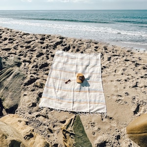 Beach blanket made from upcycled cotton, perfect for beach days, picnics, or yoga. This colorful Mexican blanket is a versatile outdoor blanket, ideal for summer adventures, camping, or as a cozy home decor throw. Soft, lightweight, and eco-friendly, it doubles as a boho throw blanket, blanket gift, or decorative layer for any coastal space. Handwoven by artisans, this sustainable, upcycled cotton blanket adds comfort and style wherever it goes.