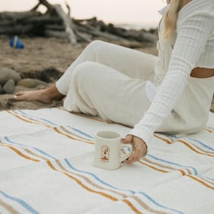 Beach blanket made from upcycled cotton, perfect for beach days, picnics, or yoga. This colorful Mexican blanket is a versatile outdoor blanket, ideal for summer adventures, camping, or as a cozy home decor throw. Soft, lightweight, and eco-friendly, it doubles as a boho throw blanket, blanket gift, or decorative layer for any coastal space. Handwoven by artisans, this sustainable, upcycled cotton blanket adds comfort and style wherever it goes.