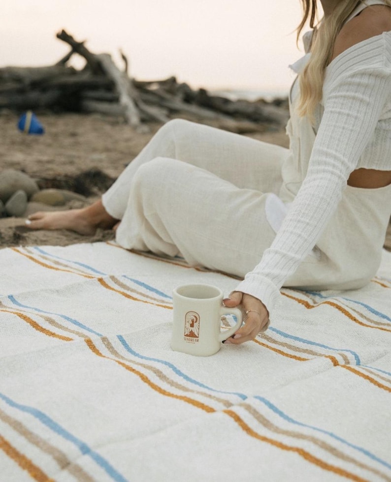 Beach blanket made from upcycled cotton, perfect for beach days, picnics, or yoga. This colorful Mexican blanket is a versatile outdoor blanket, ideal for summer adventures, camping, or as a cozy home decor throw. Soft, lightweight, and eco-friendly, it doubles as a boho throw blanket, blanket gift, or decorative layer for any coastal space. Handwoven by artisans, this sustainable, upcycled cotton blanket adds comfort and style wherever it goes.