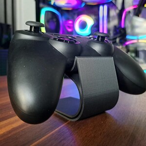 Könnte beinhalten: Ein schwarzer Gaming-Controller-Ständer mit strukturierter Oberfläche. Der Ständer ist so konzipiert, dass er einen Controller aufrecht hält.