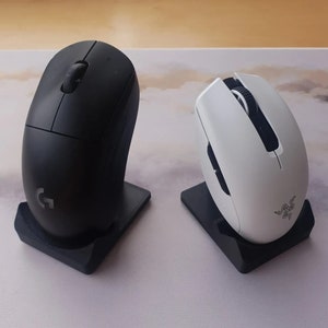 May include: Two wireless computer mice, one black and one white, are displayed on their charging stands. The mice are both ergonomic and have a sleek design.