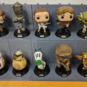 Peut inclure: Une collection de 12 figurines Star Wars Pop! Vinyl exposées sur une étagère. Les figurines incluent des personnages tels que Yoda, Chewbacca, Rey et BB-8.