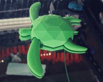 Peut inclure: Une figurine de tortue verte imprimée en 3D avec un design géométrique. La tortue fait face à la caméra, la tête et les pattes visibles.