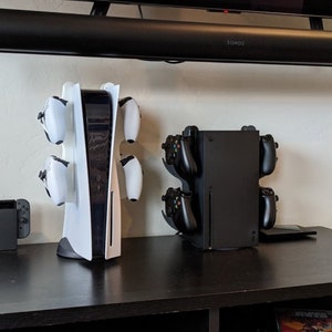 May include: A white PlayStation 5 console with a vertical stand and four white controllers. A black Xbox Series X console with a vertical stand and four black controllers. A black Nintendo Switch console.