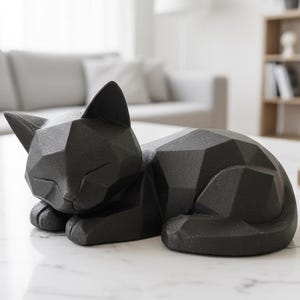 May include: A black geometric cat sculpture resting on a white marble table. The cat is in a sleeping position, with its eyes closed and paws tucked in. The sculpture has a modern, angular design. Home decor.