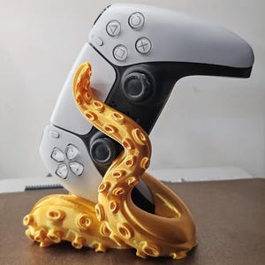 May include: A gold 3D printed octopus stand holding a white video game controller.