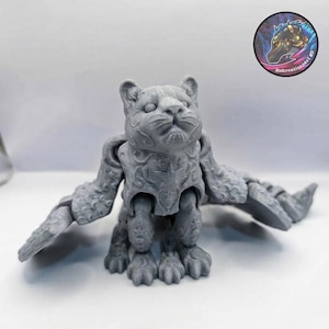May include: A gray 3D-printed articulated cat figurine with detailed wing-like appendages. The cat has intricate patterns on its body and is posed with its wings extended. The figurine is on a white surface.