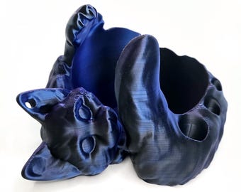 May include: A blue 3D printed cat-shaped holder with a hollowed-out center for storing items. The cat is lying on its back with its paws in the air.