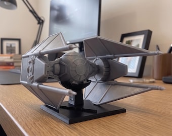 May include: A gray plastic model of a TIE Interceptor starfighter featuring a central spherical cockpit flanked by two large, angular solar array wings. The model is mounted on a black, triangular display stand that supports the craft's base.
