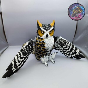 Puede incluir: Una figurita de b&uacute;ho pintada a mano con marcas negras, blancas y amarillas. El b&uacute;ho tiene las alas extendidas y est&aacute; sentado sobre una superficie blanca.