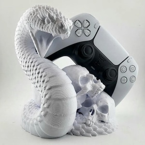 May include: A white 3D printed sculpture of a snake, skull, and a white and black video game controller. The snake is coiled around the skull and the controller is resting on top of the skull.