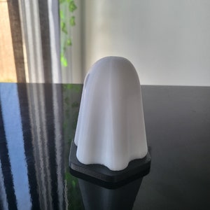 Puede incluir: Una figurita blanca en forma de fantasma con una base negra. La figurita est&aacute; hecha de un material liso y mate y tiene un dise&ntilde;o simple y moderno.