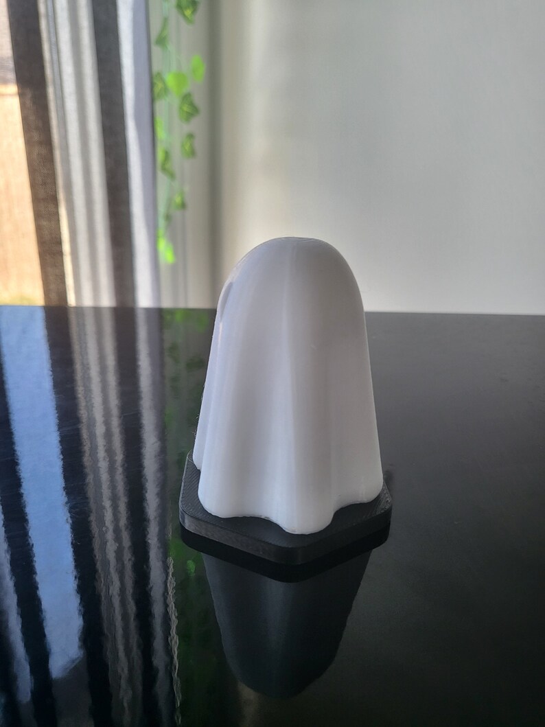 Puede incluir: Una figurita blanca en forma de fantasma con una base negra. La figurita est&aacute; hecha de un material liso y mate y tiene un dise&ntilde;o simple y moderno.