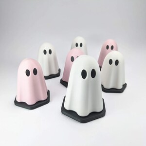 Puede incluir: Un grupo de siete figuras de fantasmas, algunas son blancas y otras rosas. Los fantasmas tienen ojos negros y est&aacute;n sentados sobre bases hexagonales negras.
