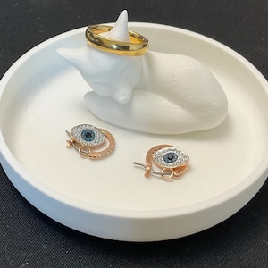 May include: White ceramic cat ring holder with a gold ring and two blue eye earrings with crystal accents.