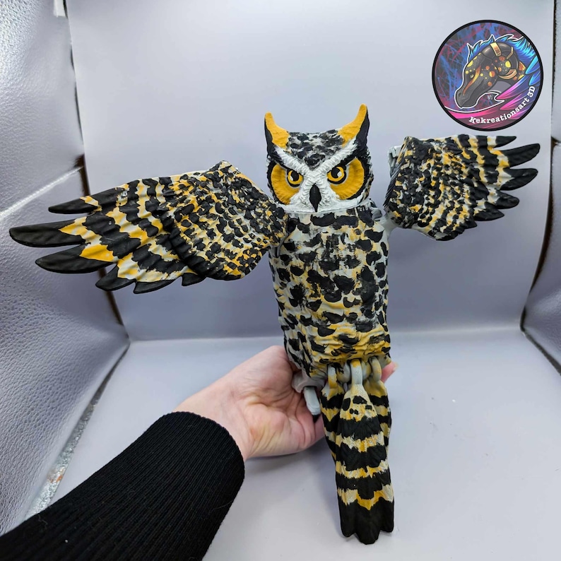 Puede incluir: Una figurita de b&uacute;ho pintada a mano con marcas negras, blancas y amarillas. El b&uacute;ho tiene las alas extendidas y est&aacute; posado sobre una superficie.