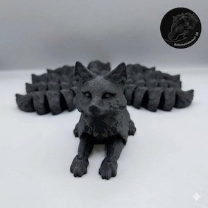 Puede incluir: Una figura de zorro negro impresa en 3D con una cola multisegmentada. El zorro está en posición sentada, con las patas delanteras extendidas. La cola se abre en abanico detrás de él. La figura tiene rasgos faciales detallados y una superficie texturizada.