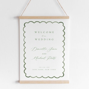 May include: A white sign with a green border hangs on a wall. The sign says "Welcome to our Wedding" with the names "Denielle Jones and Michael Potts" and the date "12.12.XX" and location "New York, New York".