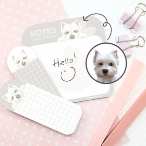 May include: A set of dog-themed sticky notes with a white and grey grid pattern. The notes feature illustrations of a West Highland White Terrier and the text "Hello!". Pink and grey office supplies are also visible.