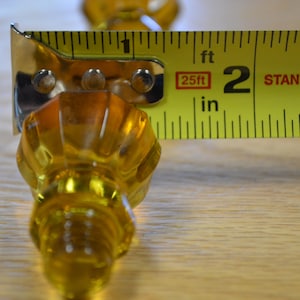 May include: A yellow glass knob with a fluted design is measured with a yellow tape measure. The tape measure reads 2 inches.