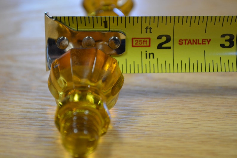 May include: A yellow glass knob with a fluted design is measured with a yellow tape measure. The tape measure reads 2 inches.