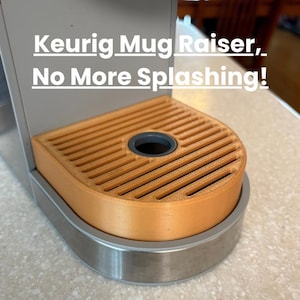 Puede incluir: Un elevador de tazas Keurig de color naranja claro con un diseño ranurado, sobre una base plateada. El texto "Keurig Mug Raiser, No More Splashing!" es visible. Accesorio para máquina de café.