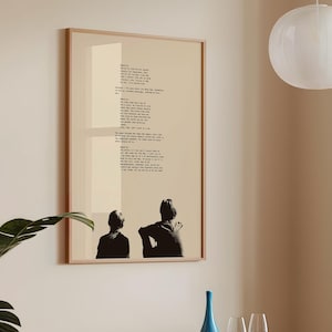 May include: A framed art print with a poem in black text on a beige background. Two silhouetted figures are at the bottom. The frame is light wood. The print hangs on a beige wall. A blue bottle and wine glasses are on a table.