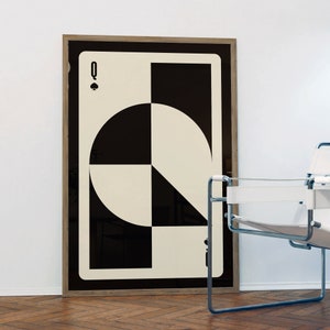 May include: A framed poster of a black and white Queen of Spades playing card with a geometric design. The card is framed in a light wood frame.