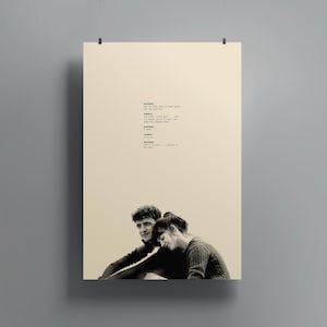 Puede incluir: Un póster en tonos sepia que muestra a una pareja abrazándose, con texto de un guion encima. El hombre tiene el pelo oscuro y rizado, y la mujer apoya la cabeza en su hombro. El póster está suspendido por una pinza en la parte superior.