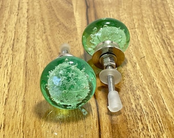 May include: Two green glass cabinet knobs with silver metal bases and screws. The knobs have a bubbly texture.
