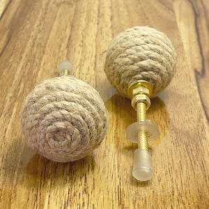 May include: Two brown rope drawer pulls with gold metal hardware. The pulls are made of natural rope and have a rustic look.