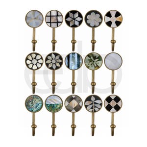 May include: A collection of decorative wall hooks with brass stems and circular tops. The tops feature various inlaid designs, including geometric patterns, floral motifs, and iridescent shell accents. Each hook is designed for hanging items.