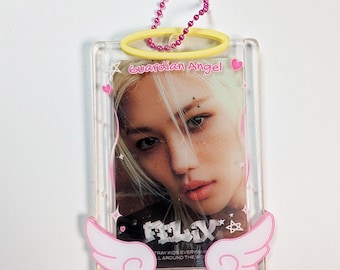 May include: A clear rectangular plastic photo holder featuring a portrait of a person with blonde hair. The holder is decorated with a yellow halo at the top, pink angel wings at the bottom, and a pink ball chain. Text reads Guardian Angel and FELIX.