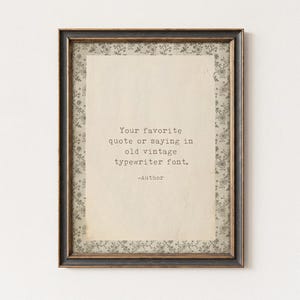 May include: A rectangular wall frame with a dark, distressed finish containing a cream-colored paper insert. The insert features a floral border and the black text: Your favorite quote or saying in old vintage typewriter font. -Author
