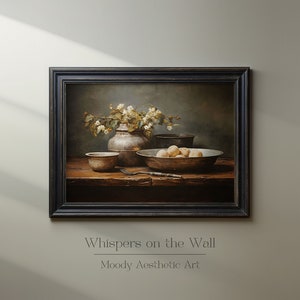 May include: A still life painting depicting a silver vase filled with white flowers, a bowl of fruit, and other antique kitchenware on a wooden table. The painting is framed in a dark wood frame and has a moody aesthetic.