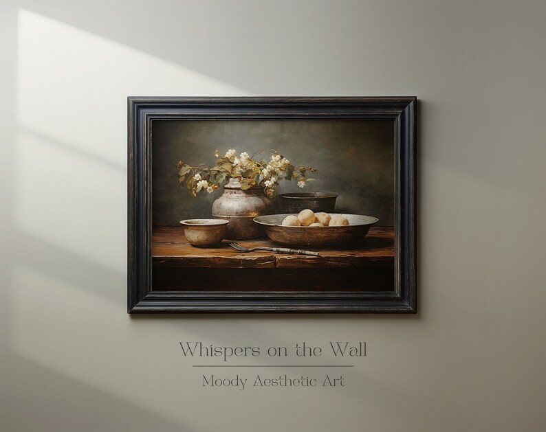 May include: A still life painting depicting a silver vase filled with white flowers, a bowl of fruit, and other antique kitchenware on a wooden table. The painting is framed in a dark wood frame and has a moody aesthetic.