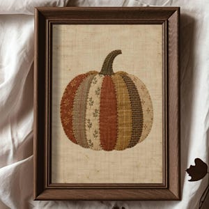 Peut inclure: Une impression d'art encadrée représentant une illustration de citrouille composée de bandes verticales aux tons orange, marron, beige et crème. La citrouille possède une tige verte texturée sur un fond beige clair dans un cadre en bois foncé.