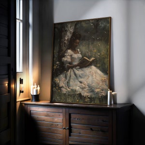 May include: A framed painting of a woman in a white dress sitting in a field of flowers and reading a book. The painting is set against a dark green background.