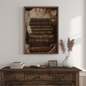 May include: A framed portrait of a woman wearing a pearl necklace and holding a stack of antique books in front of her chest.