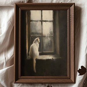 May include: A framed painting of a white cat sitting on a windowsill, looking out a window with rain falling outside. The painting is in a dark brown frame.