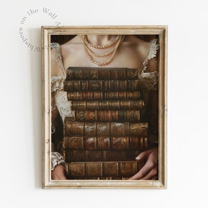 May include: A framed print depicting a woman holding a stack of antique books in front of her chest. The books are bound in brown leather with gold accents and feature intricate designs on the covers. The woman is wearing a white lace dress and a pearl necklace.