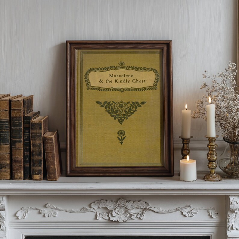 May include: A framed print with a yellow background and green text that reads "Marcelene & the Kindly Ghost". The print is surrounded by a dark brown frame and is displayed on a white mantel with two candlesticks and candles.