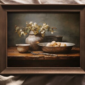 May include: A still life painting in a brown frame shows a rustic wooden table with a bowl of potatoes, a small bowl, a vase of white flowers, and a fork. The background is a muted green.