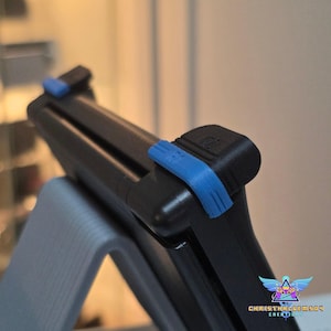 May include: A black handheld gaming console accessory featuring bright blue plastic clips attached to the top edges. The device is mounted on a light gray stand. The text "CHRISTHALGEM504 CREATIONS" is visible in the bottom right corner.